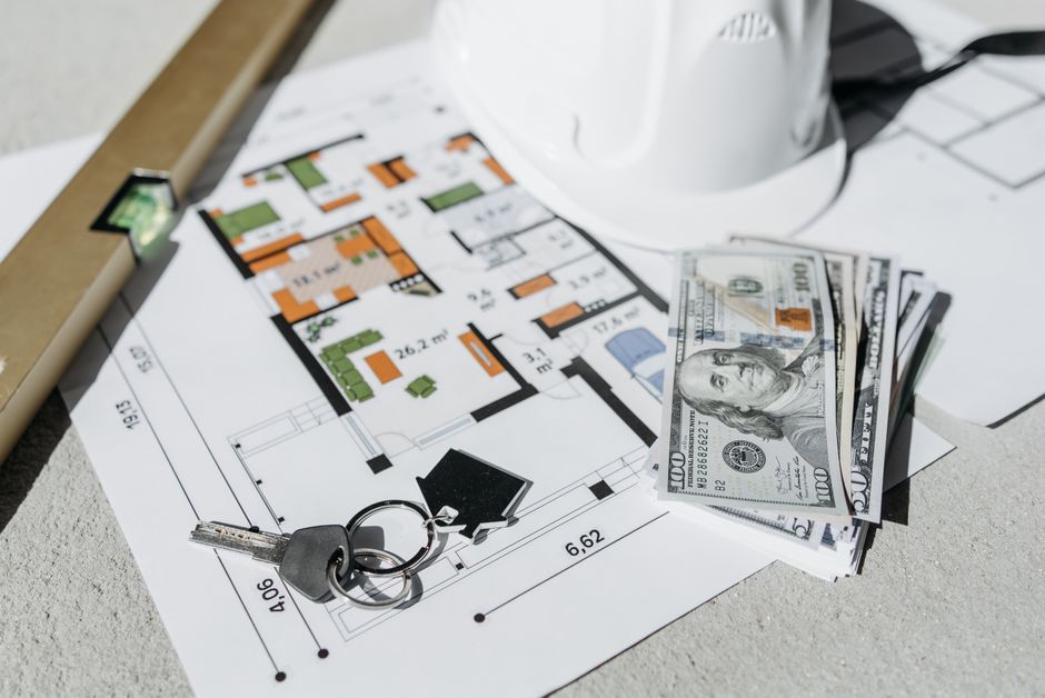 Floor plan with cash, keys, and hard hat symbolizing real estate investment and property planning.